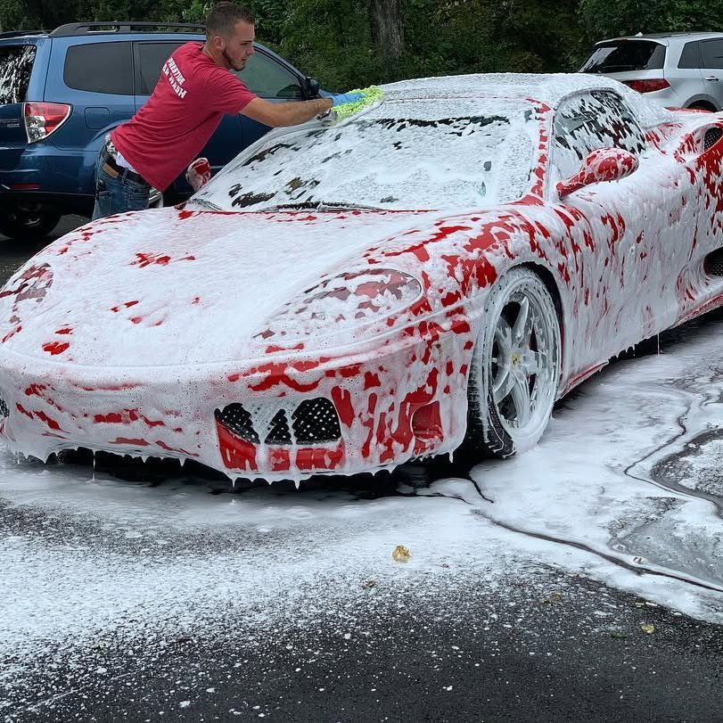 Prestige team member hand washing a red Ferrari with thick foam at the Hopewell Junction location