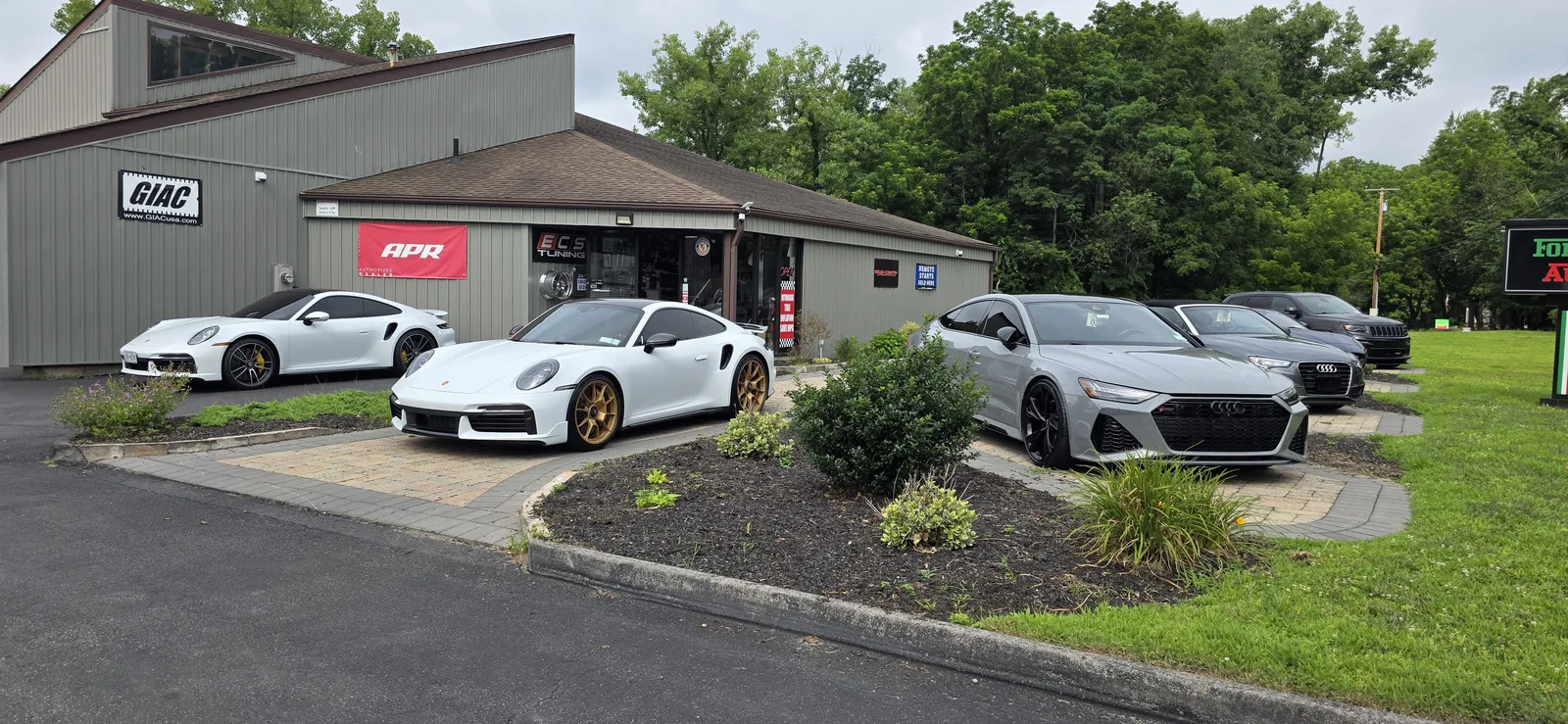 Prestige Performance Center — Formula One Autosport building with Porsche 911 Turbos and Audi RS7 out front